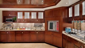 A kitchen with wooden cabinets, a microwave, a grill, a stainless steel oven, and a beverage dispenser.