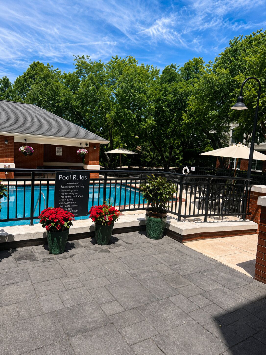 A pool area with a sign listing pool rules, a brick building, and a fenced patio with potted plants.