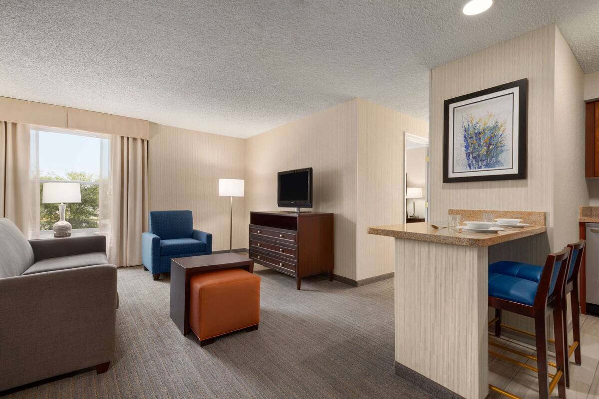 A hotel room with a living area, a TV, a minibar, and a dining area.