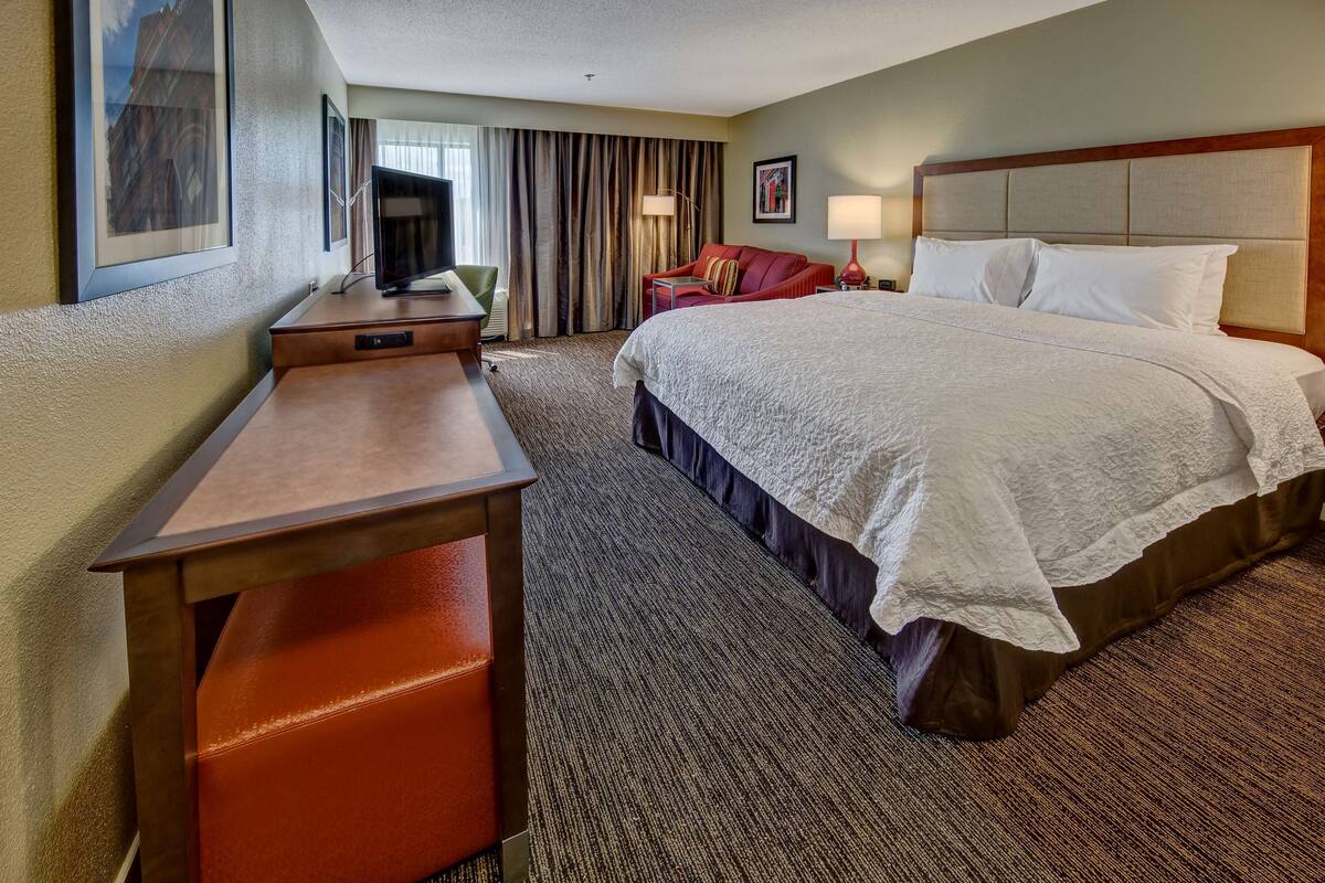 A hotel room with a large bed, a desk with a chair, a television, and a red sofa.