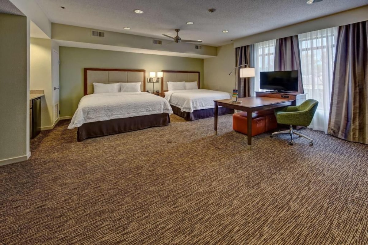 A hotel room with two beds, a desk, a television, and a chair.
