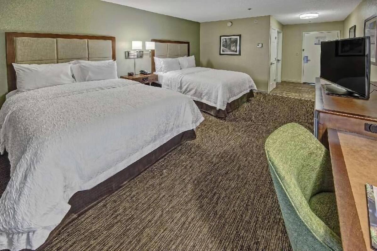 A hotel room with two beds, a desk with a television, and a green chair.