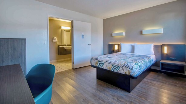 A modern hotel room with a large bed, a desk, and a chair. There is a bathroom visible through an open door. - Motel 6 Santa Fe (Santa Fe)
