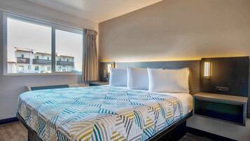 A hotel room with a large bed, a nightstand, a bedside table, and a window with a view of buildings.