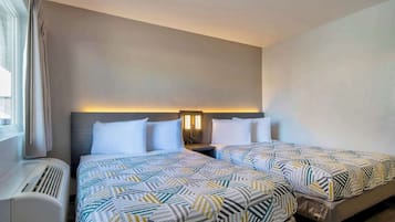 Een hotelkamer met twee bedden, een nachtkastje, een lamp en een raam met gordijnen.