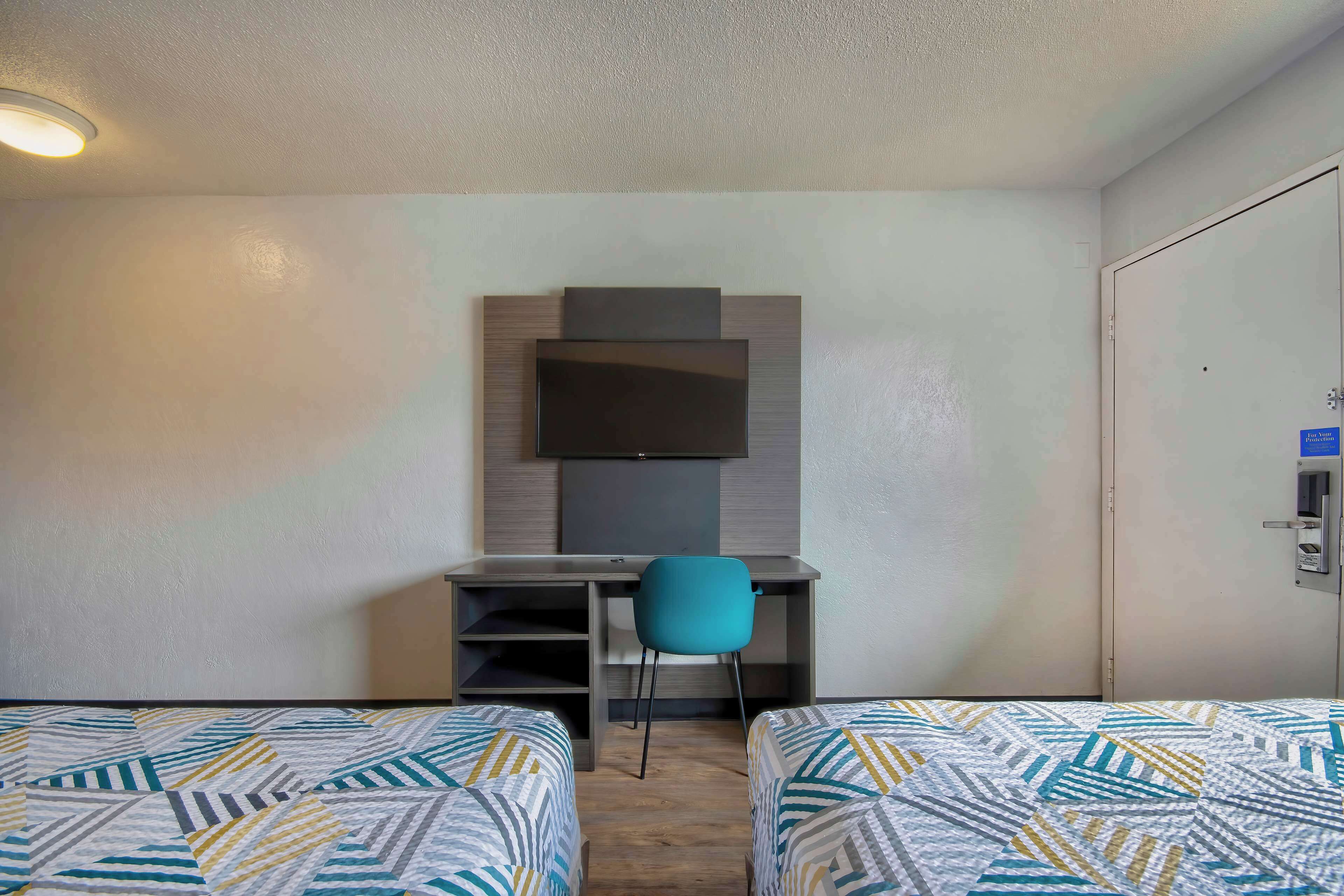 A hotel room with two beds, a desk, a chair, and a television mounted on the wall.