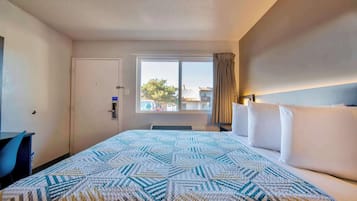 Habitación de hotel con una cama grande, un escritorio y una ventana con vistas a edificios y árboles.