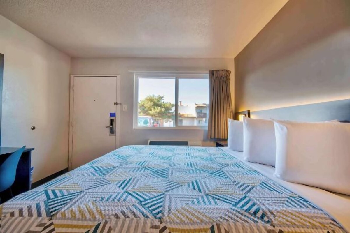 A hotel room with a bed, a desk, a window with curtains, and a view of the outside.
