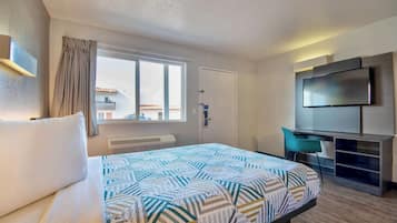 A hotel room with a bed, a desk, a chair, a TV, and a window with curtains.