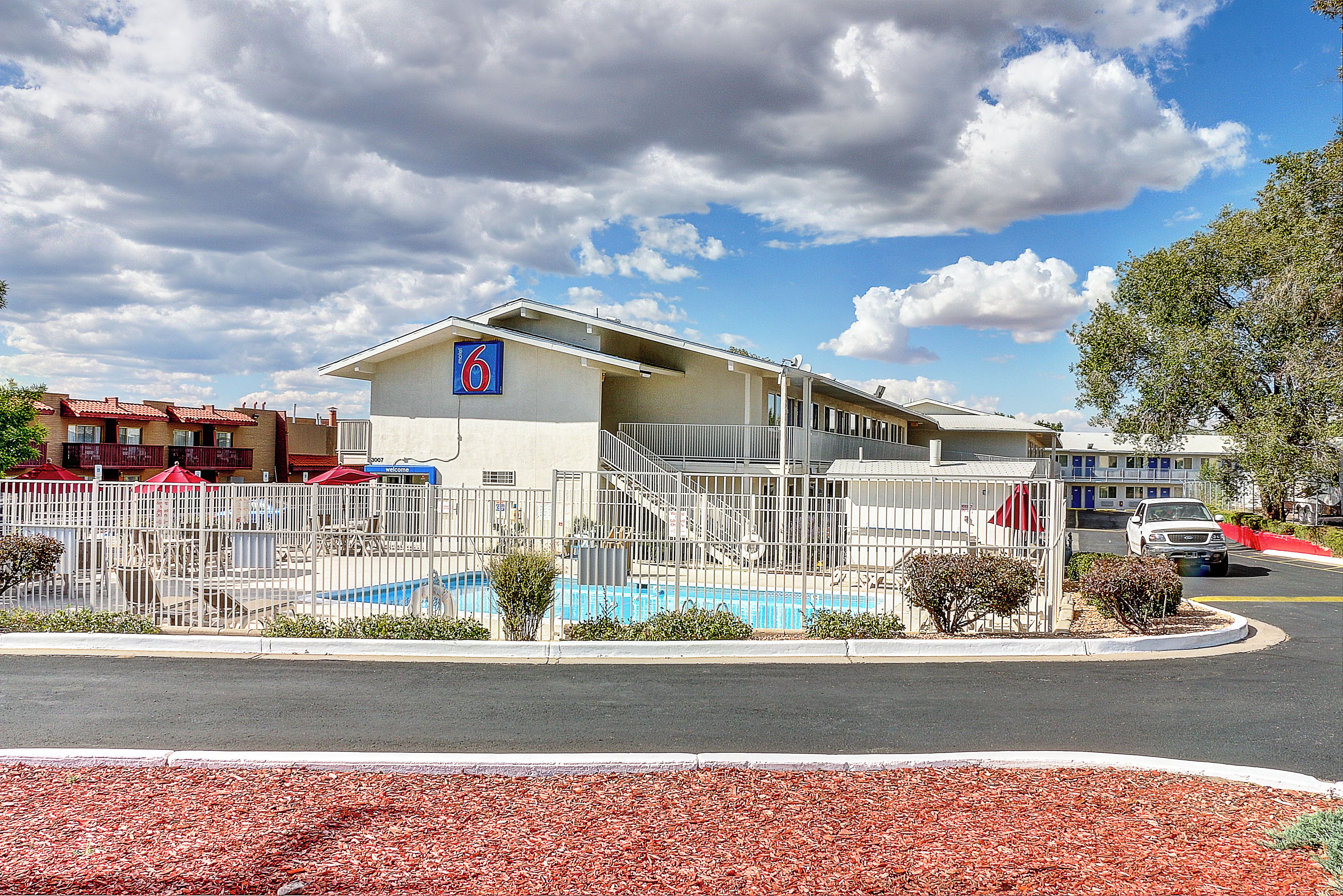 A hotel with a swimming pool, fenced area, and a parking lot.