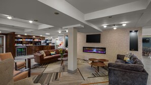 A modern hotel lobby with a seating area, a kitchen, and a flat-screen TV mounted on the wall.