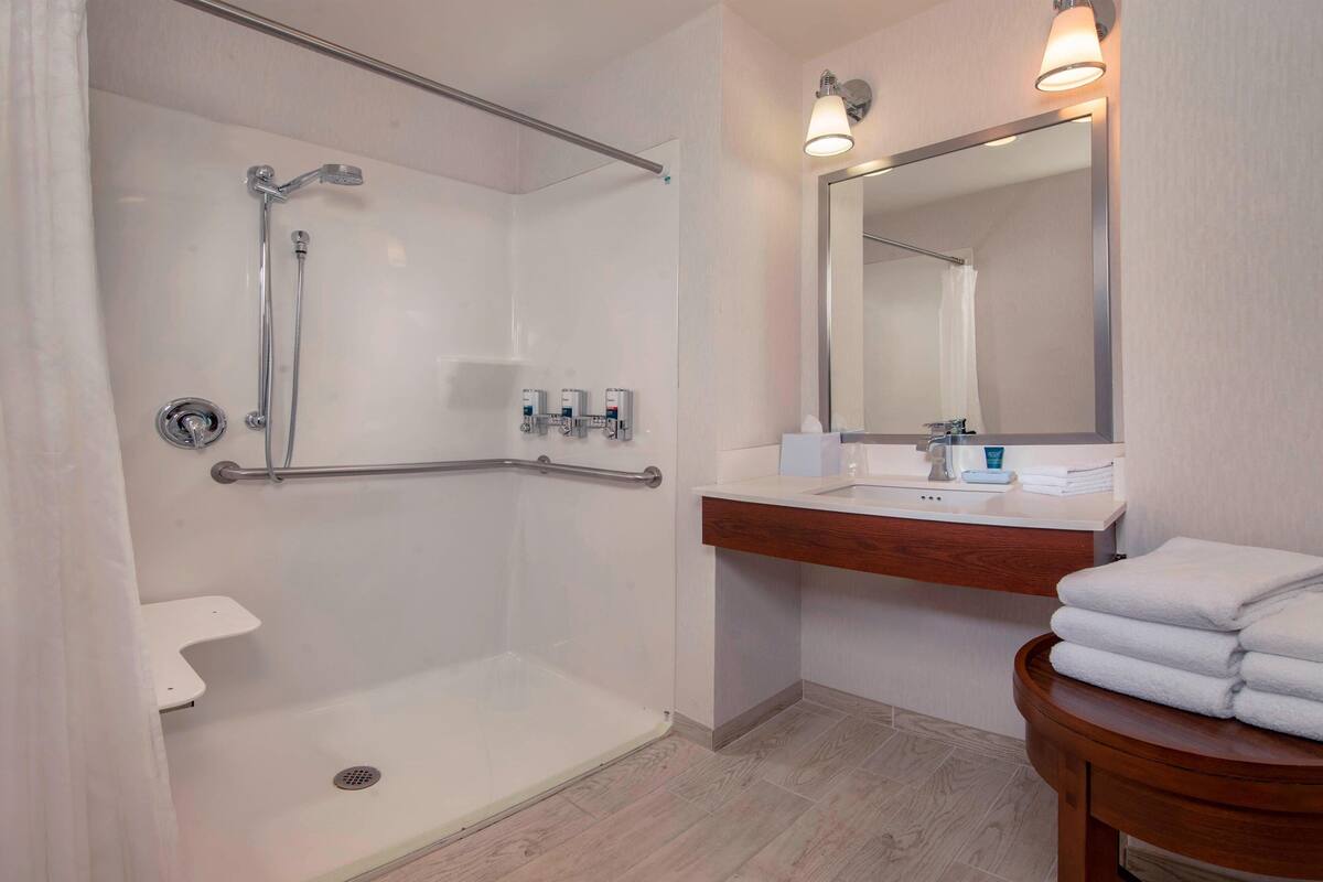 A modern bathroom with a walk-in shower, a vanity with a mirror, and a wooden side table with towels.