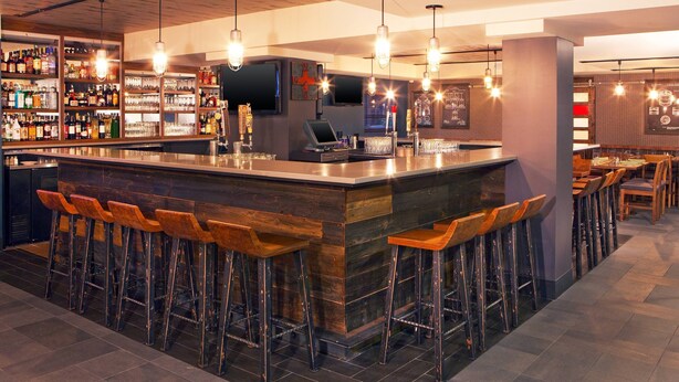 A bar area with a central island, bar stools, a television, and shelves with bottles.