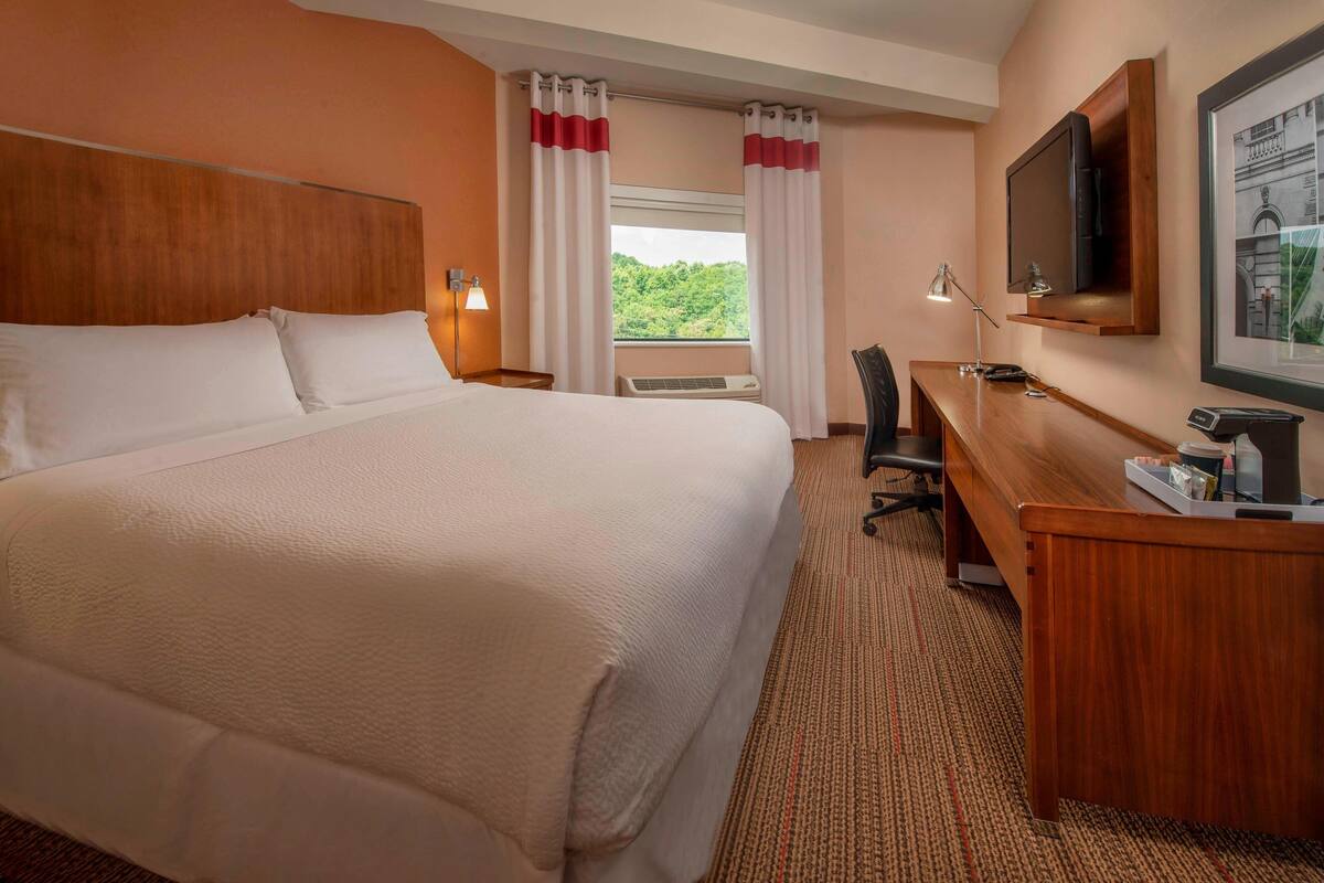 A hotel room with a large bed, a desk with a chair, a TV, and a window with curtains.