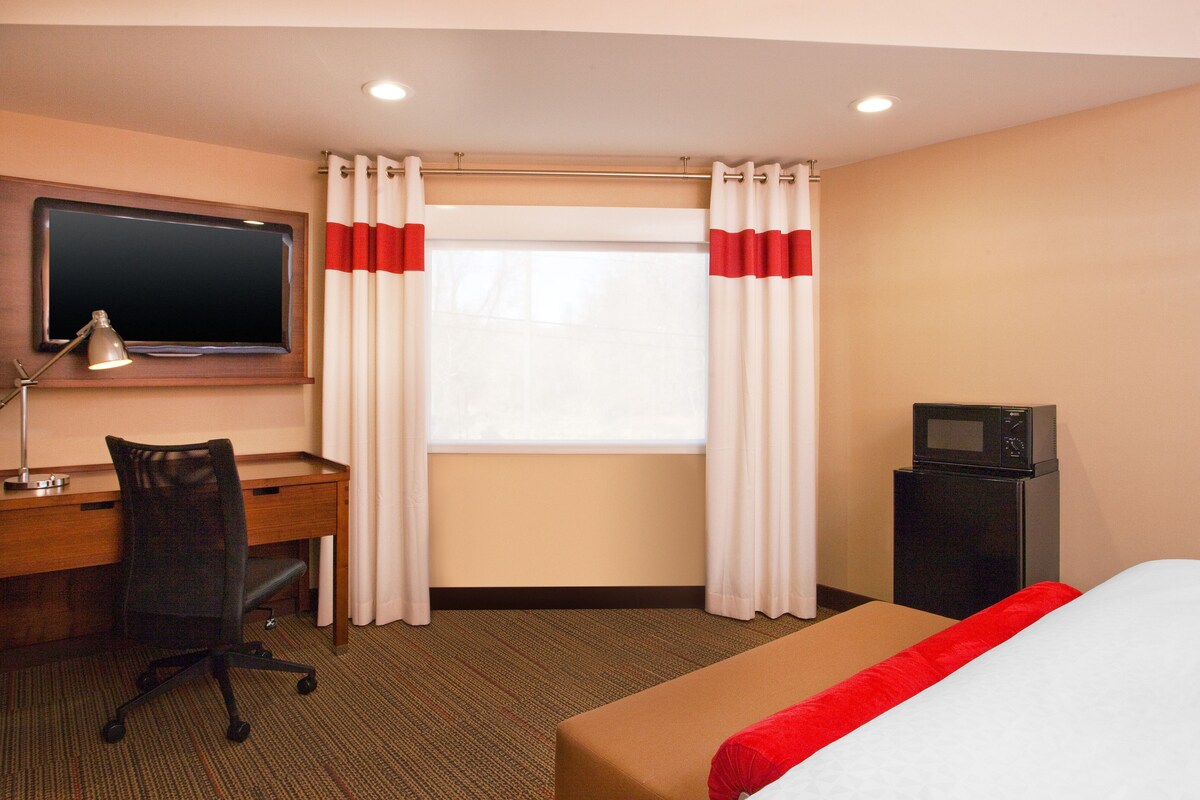 Habitación de hotel con cama, escritorio, silla, televisor y microondas.