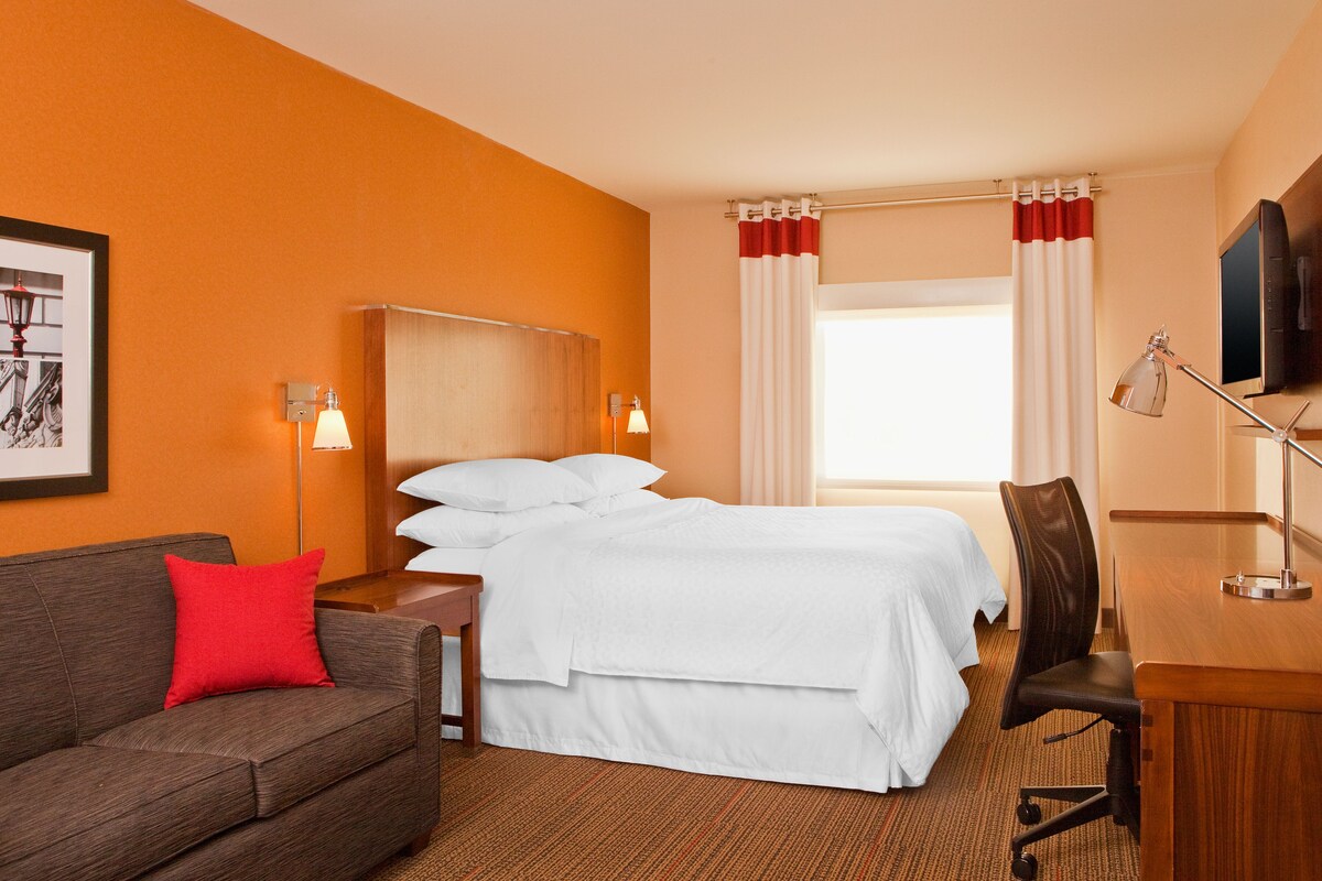 Una habitación de hotel con una cama grande, un escritorio, una silla, un sofá y una televisión.