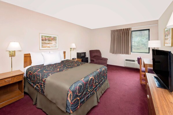 Habitación de hotel con una cama grande, dos mesitas de noche, una silla, un escritorio con televisor y una ventana con cortinas.