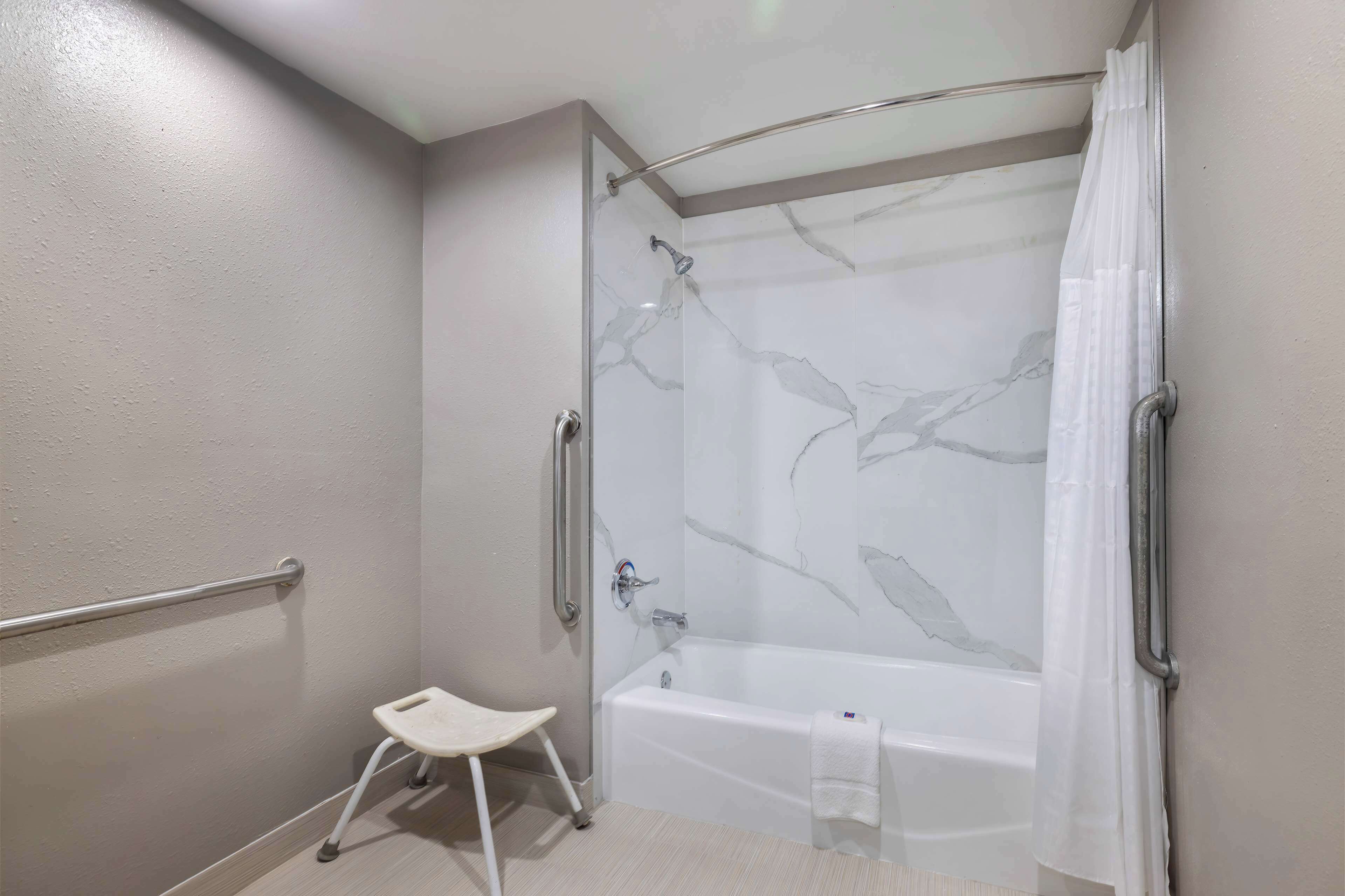 A modern bathroom with a glass-enclosed shower, a white bathtub, and a small white stool.