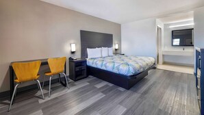 A modern hotel room with a bed, two chairs, a nightstand, and a TV mounted on the wall. - Motel 6 Lake Charles, LA (Lake Charles)