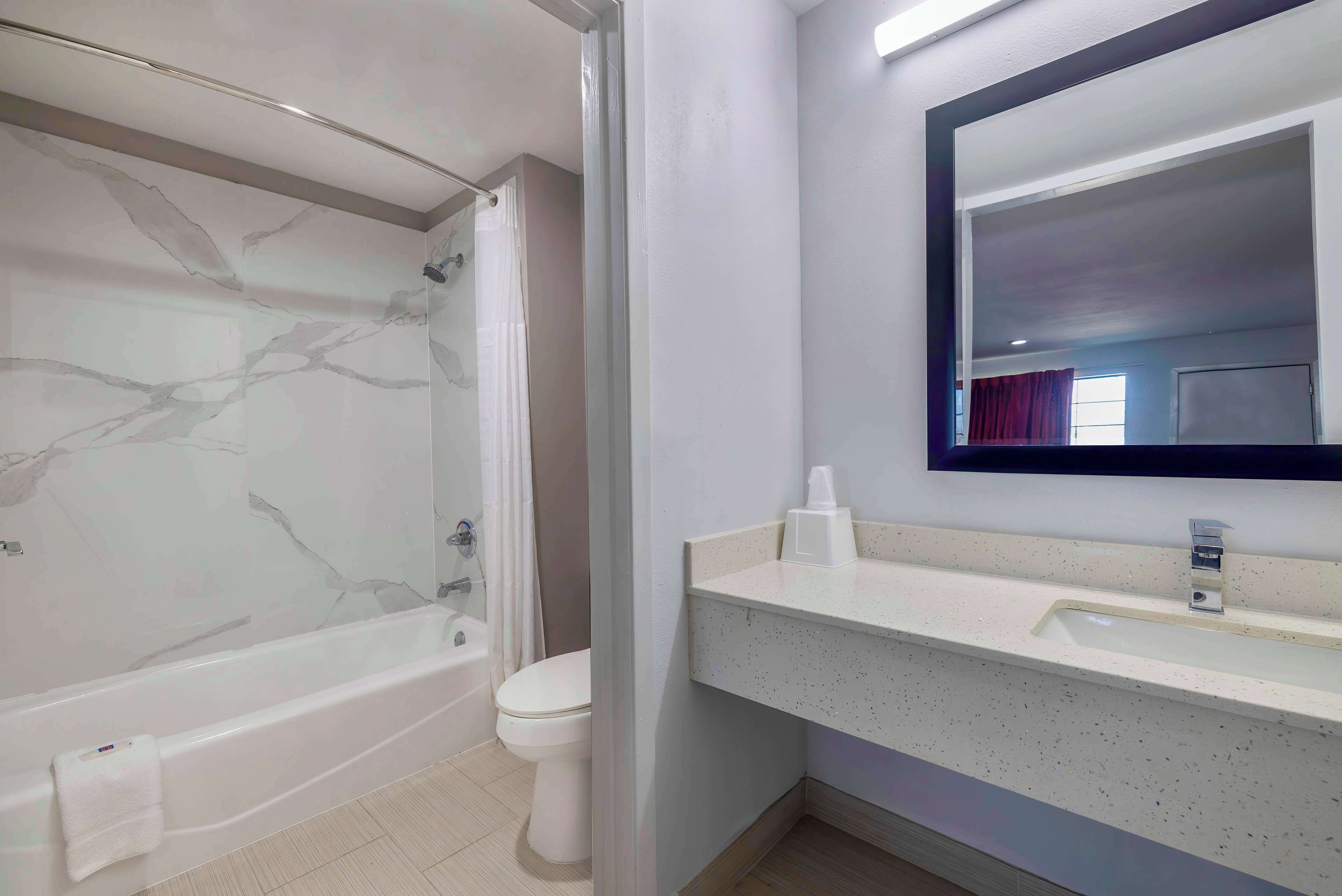 A modern bathroom with a marble shower wall, a bathtub, a toilet, and a sink with a mirror above it.