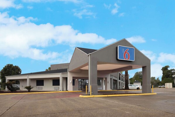 Un motel con letrero '6', estacionamiento techado y cielo despejado.