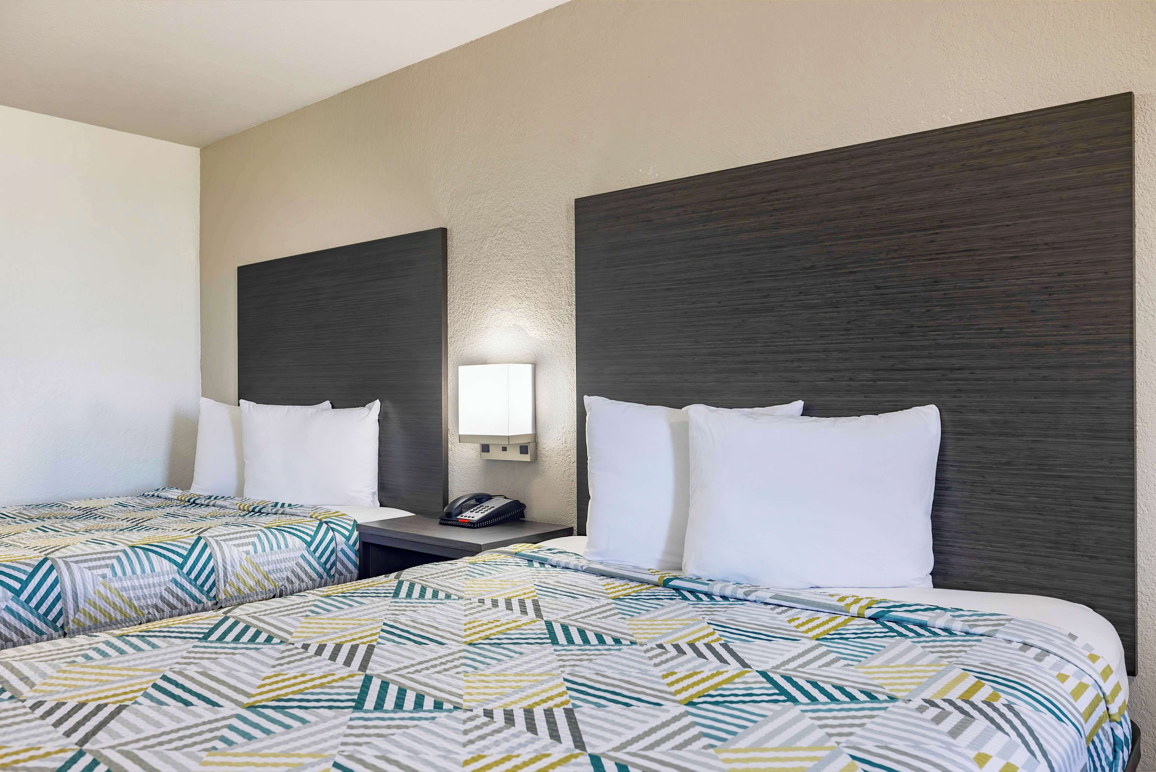 Habitación de hotel con dos camas, cada una con una colcha estampada, una mesita de noche con lámpara y teléfono.