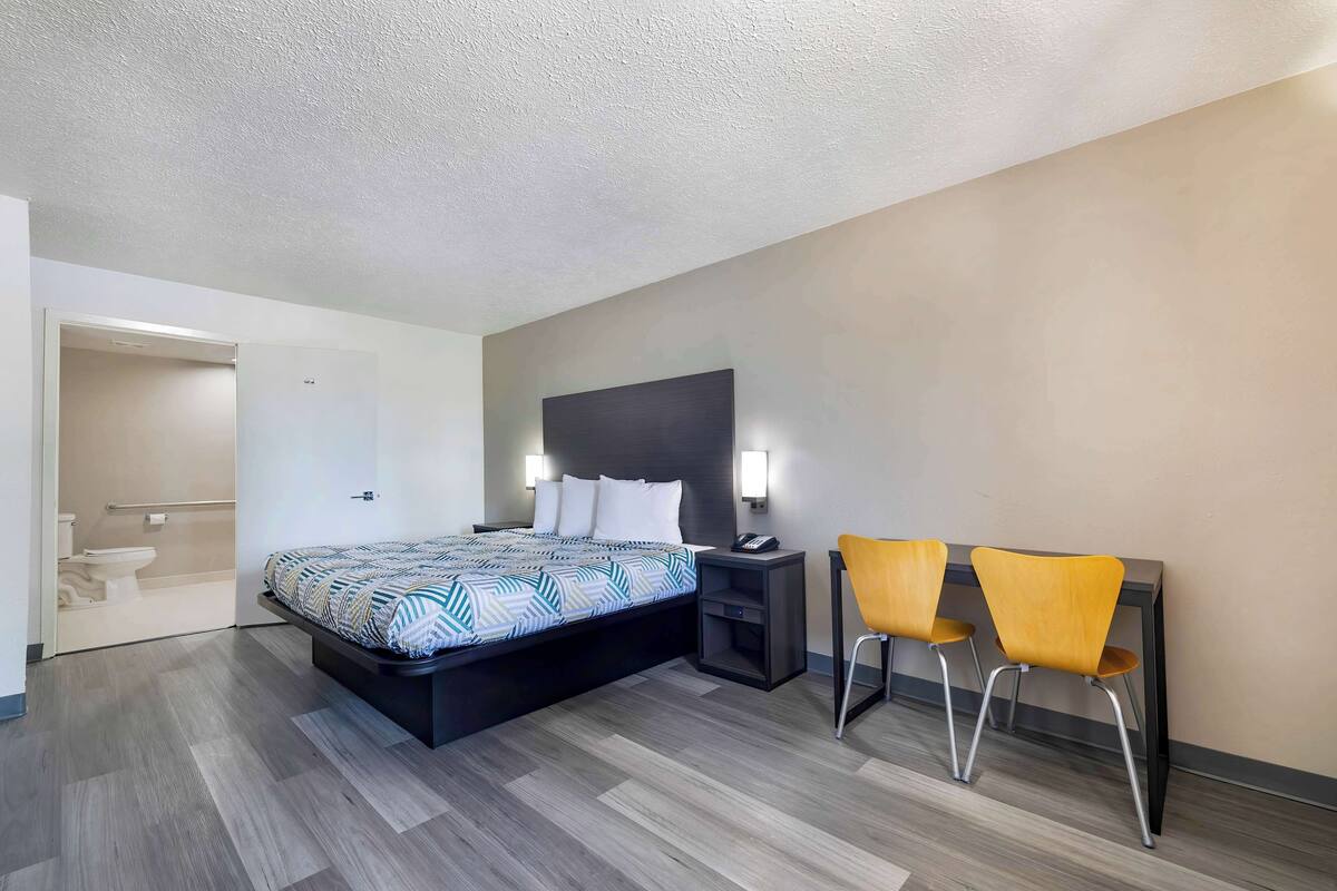 A modern hotel room with a large bed, bedside table, and a desk with two chairs.