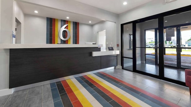 A reception area with a modern design, featuring a large number '6' on the wall, a reception desk, and a colorful striped floor. - Motel 6 Lake Charles, LA (Lake Charles)