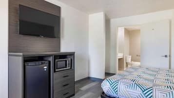 A hotel room with a bed, a TV mounted on the wall, a refrigerator, and a microwave.