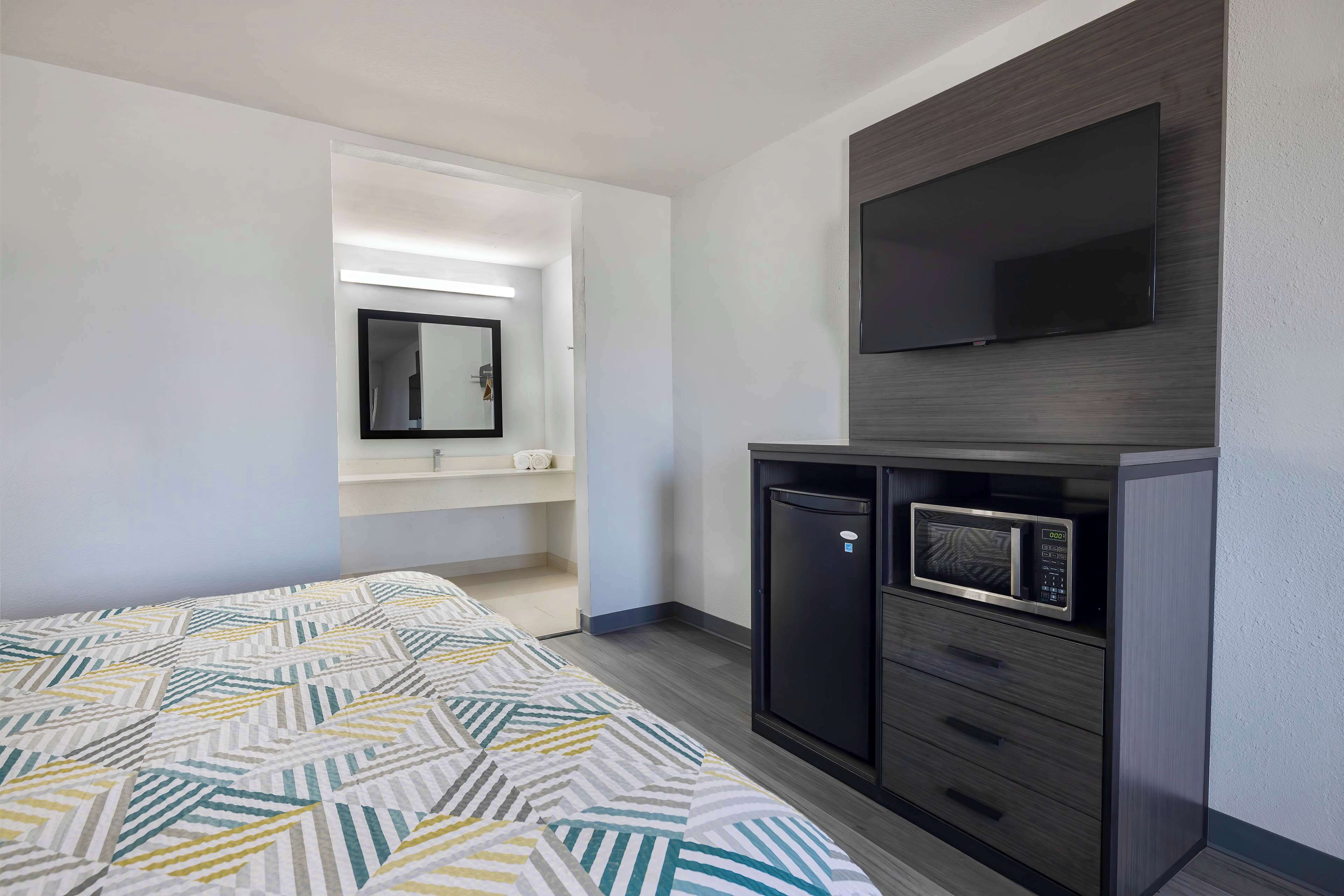 Una habitación de hotel con cama, televisión montada en la pared, microondas y un mueble pequeño.