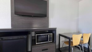 A compact kitchenette with a microwave, a small refrigerator, and a flat-screen TV mounted on the wall. There are two chairs and a small table. - Motel 6 Lake Charles, LA (Lake Charles)