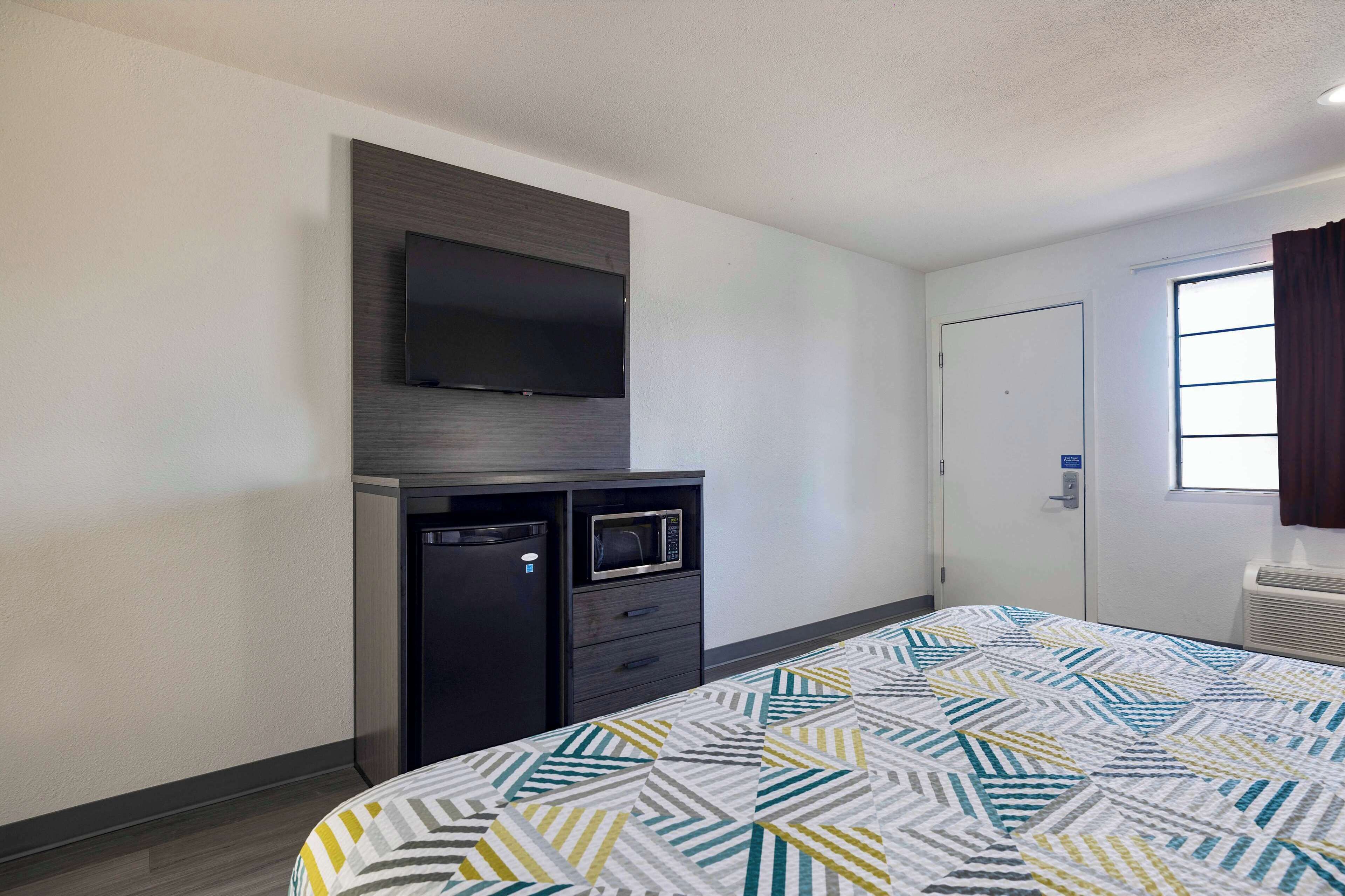 A hotel room with a bed, a flat-screen TV mounted on the wall, a microwave, and a door with a window.