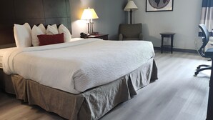 A hotel room with a large bed, a desk with a lamp, a chair, a small table, and a world map on the wall. - Ramada by Wyndham Luling (Luling)