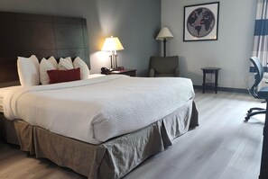 Habitación de hotel con una cama grande, un escritorio con lámpara, una silla, una mesita y un mapa del mundo en la pared.