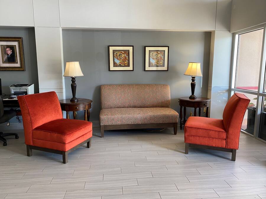 A room with a sofa, two armchairs, a desk with a printer, and two lamps.