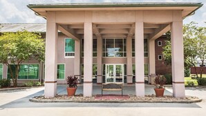 A building with a covered entrance, columns, and potted plants. - Ramada by Wyndham Luling (Luling)