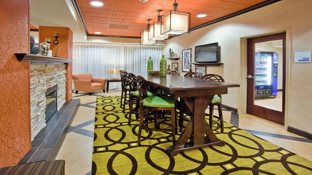 A hotel room with a dining area featuring a wooden table and chairs, a fireplace, a television, and a vending machine. - Holiday Inn Express Peachtree Corners - Norcross by IHG (Peachtree Corners)