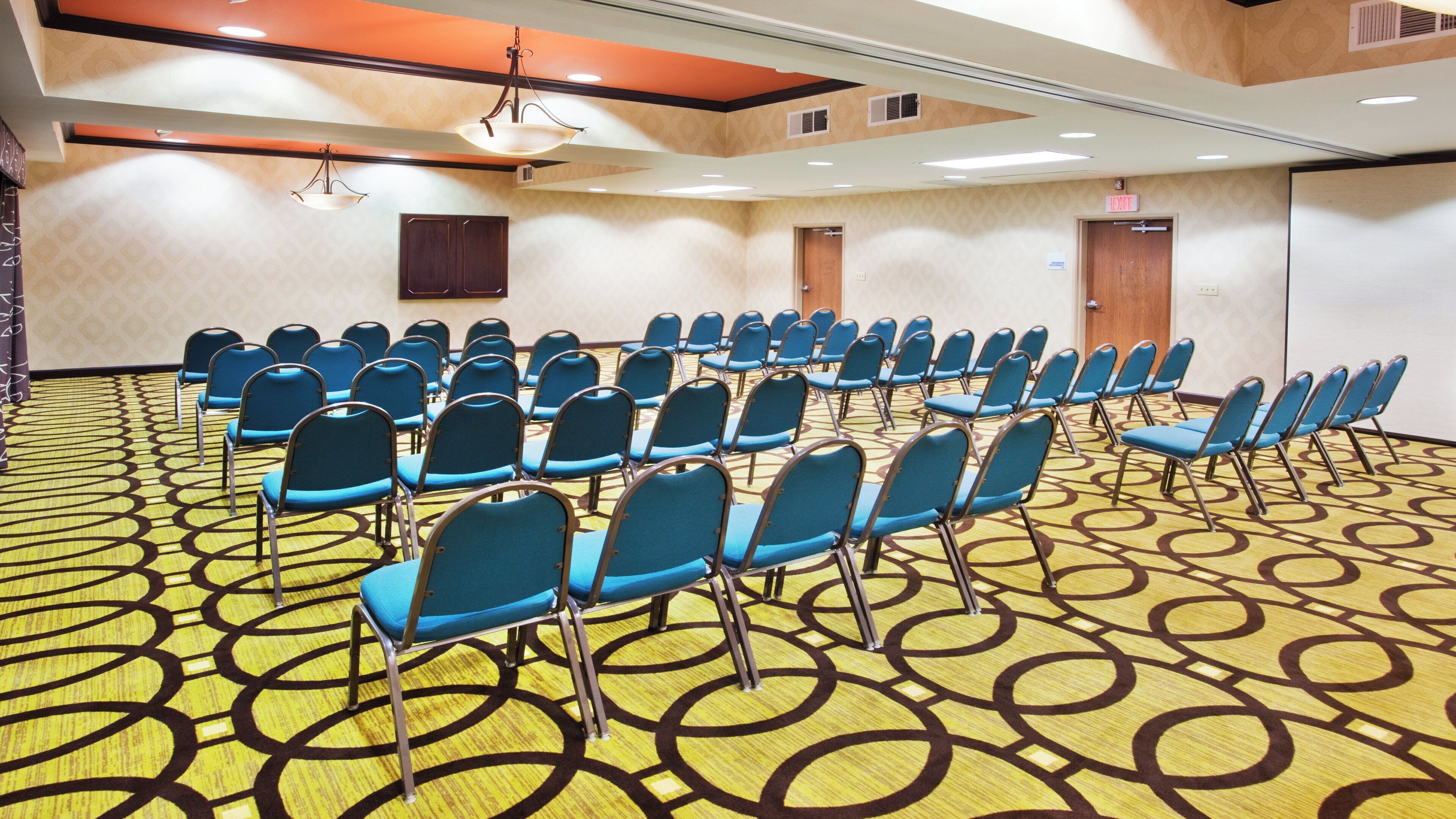 A conference room with rows of chairs, a patterned carpet, and a ceiling with recessed lighting.