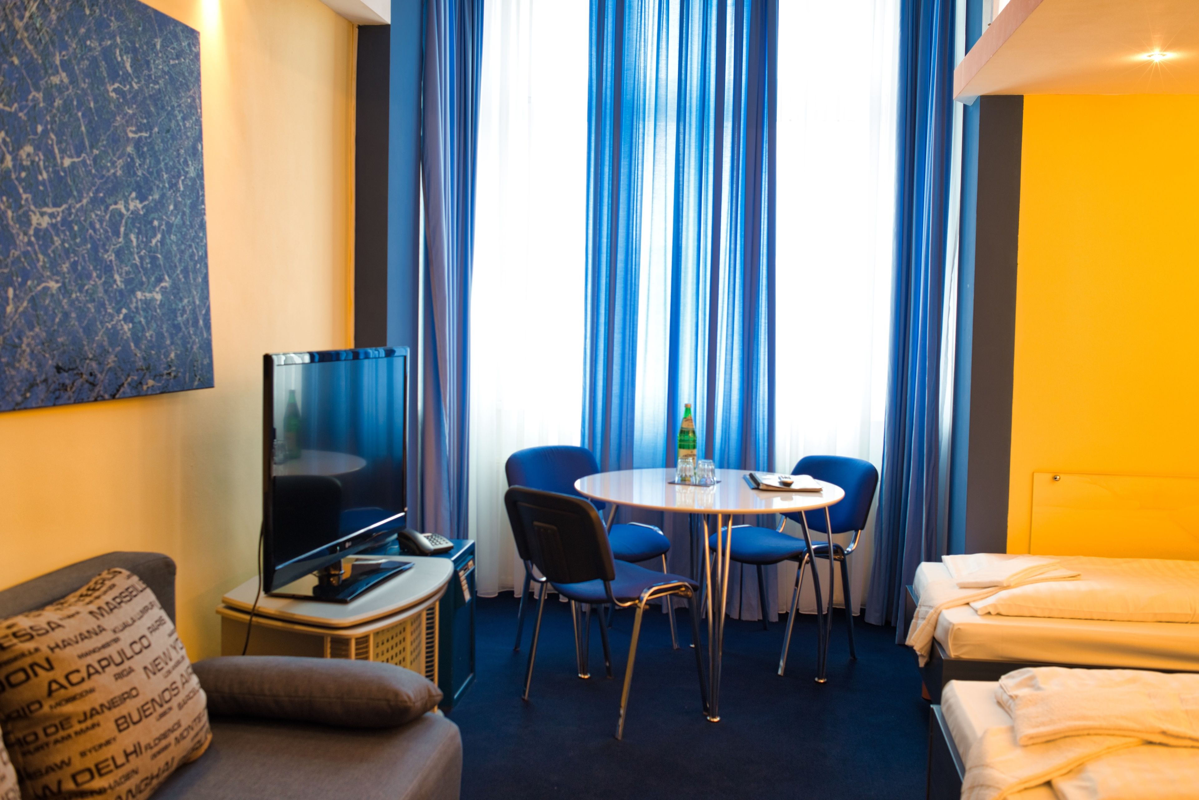 Una habitación de hotel con televisión, una mesa redonda con sillas, un sofá y una cama.