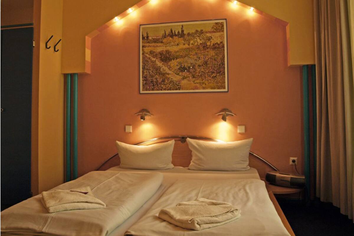 Habitación de hotel con dos camas, un cuadro en la pared y una mesita con lámpara.