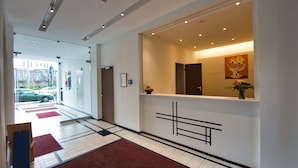 Zona de recepción de hotel con diseño moderno, que incluye un mostrador, un espejo grande y una obra de arte colgada en la pared.