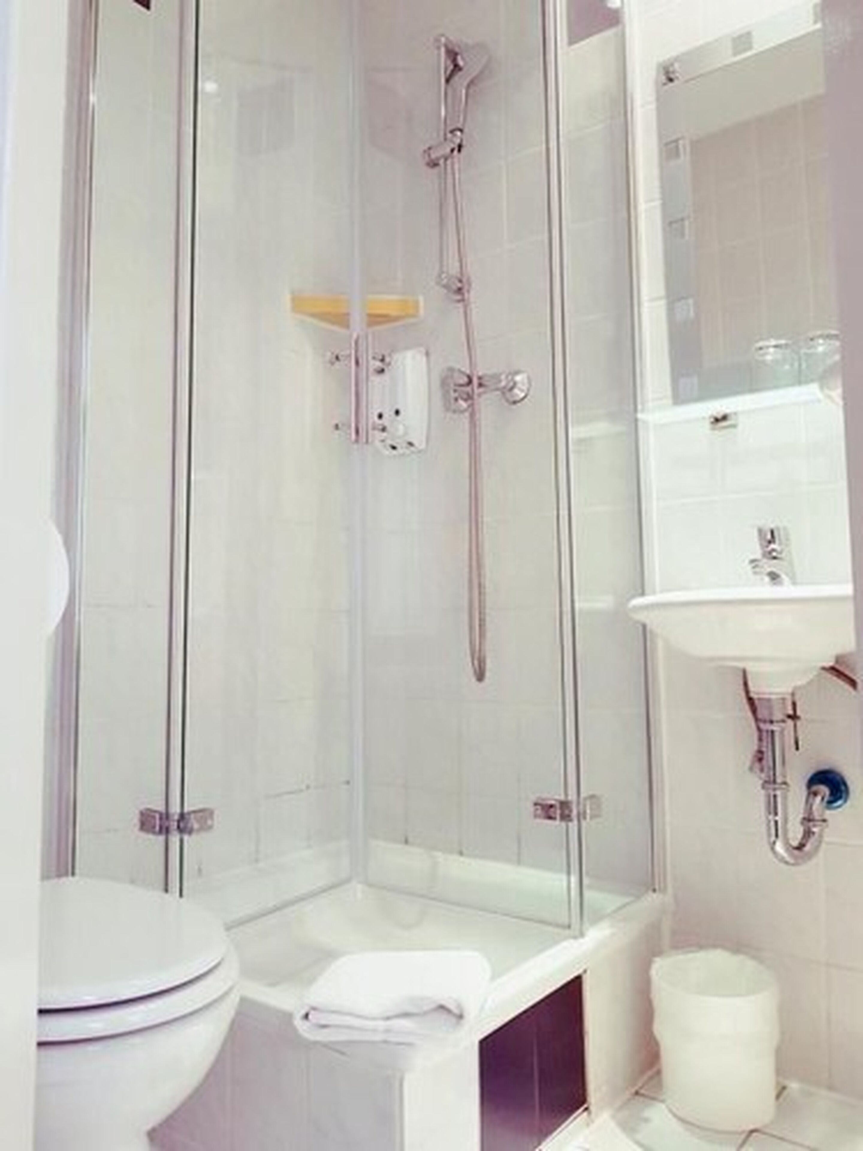 Un baño moderno con ducha envuelta en vidrio, inodoro y lavamanos con espejo.