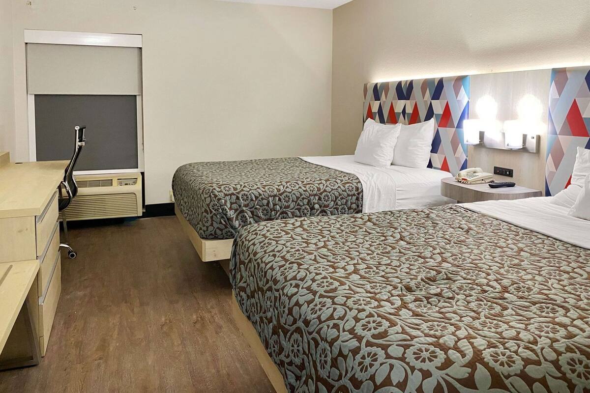 Habitación de hotel con dos camas, un escritorio, un armario y un espejo.