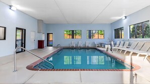 An indoor swimming pool with a tiled floor, a metal pool ladder, and white lounge chairs arranged around the pool. - Days Inn & Suites by Wyndham Peachtree Corners/Norcross (Peachtree Corners)