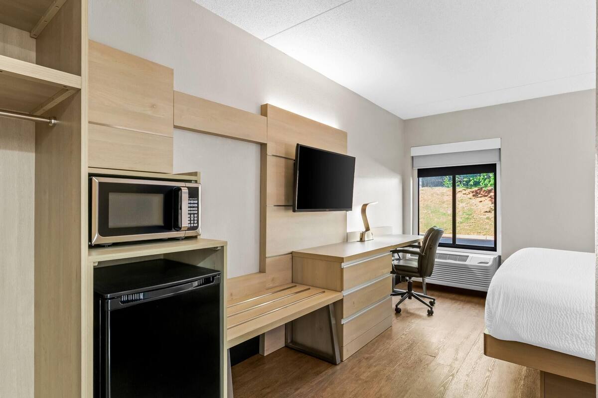 Habitación de hotel moderna con un escritorio de madera, microondas, televisor, cama y ventana con vistas.