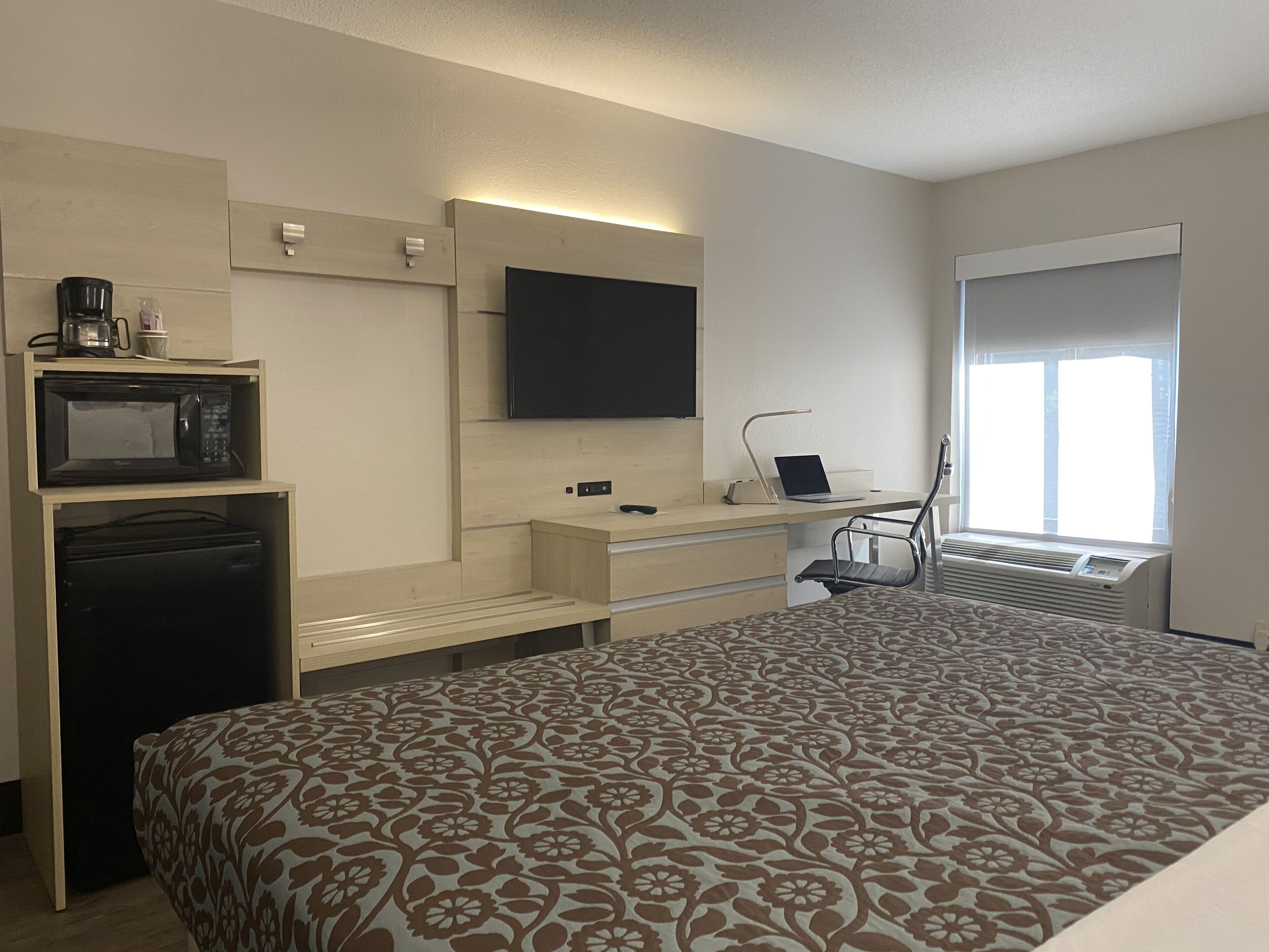Habitación de hotel con una cama, un escritorio con una computadora portátil, un televisor de pantalla plana, un microondas y una cafetera.
