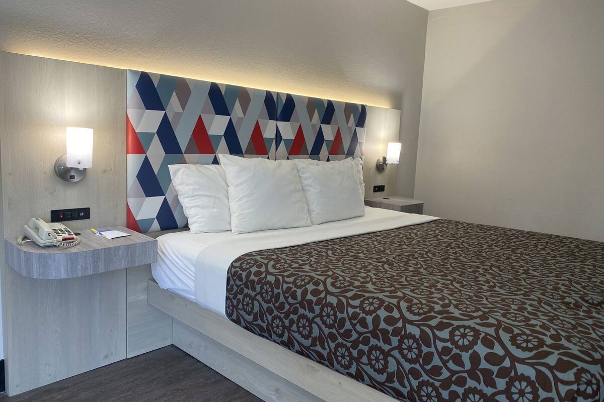 Una habitación de hotel con cama, teléfono de noche, mesita de noche y cabecera con estampado geométrico.