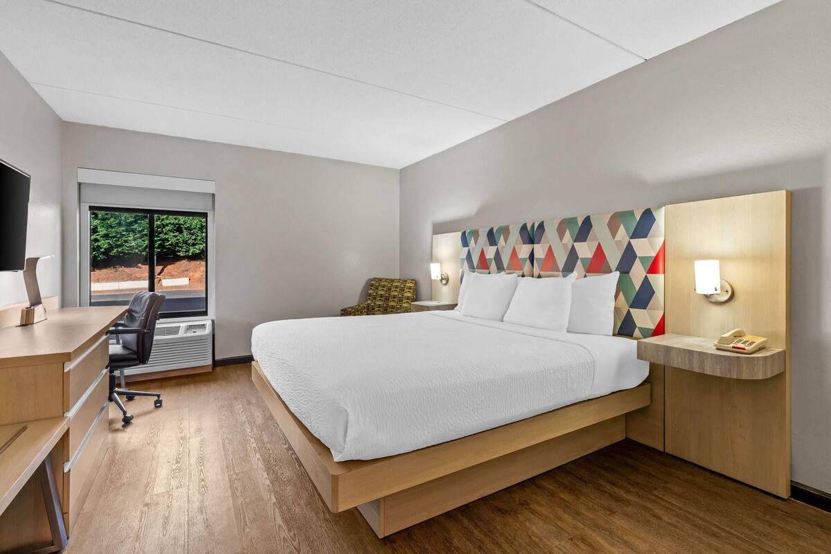 Habitación de hotel moderna con cama, escritorio, silla y ventana con vistas a árboles.