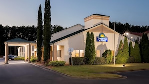 A Days Inn & Suites building with a covered entrance, a satellite dish, and a well-maintained lawn. - Days Inn & Suites by Wyndham Peachtree Corners/Norcross (Peachtree Corners)