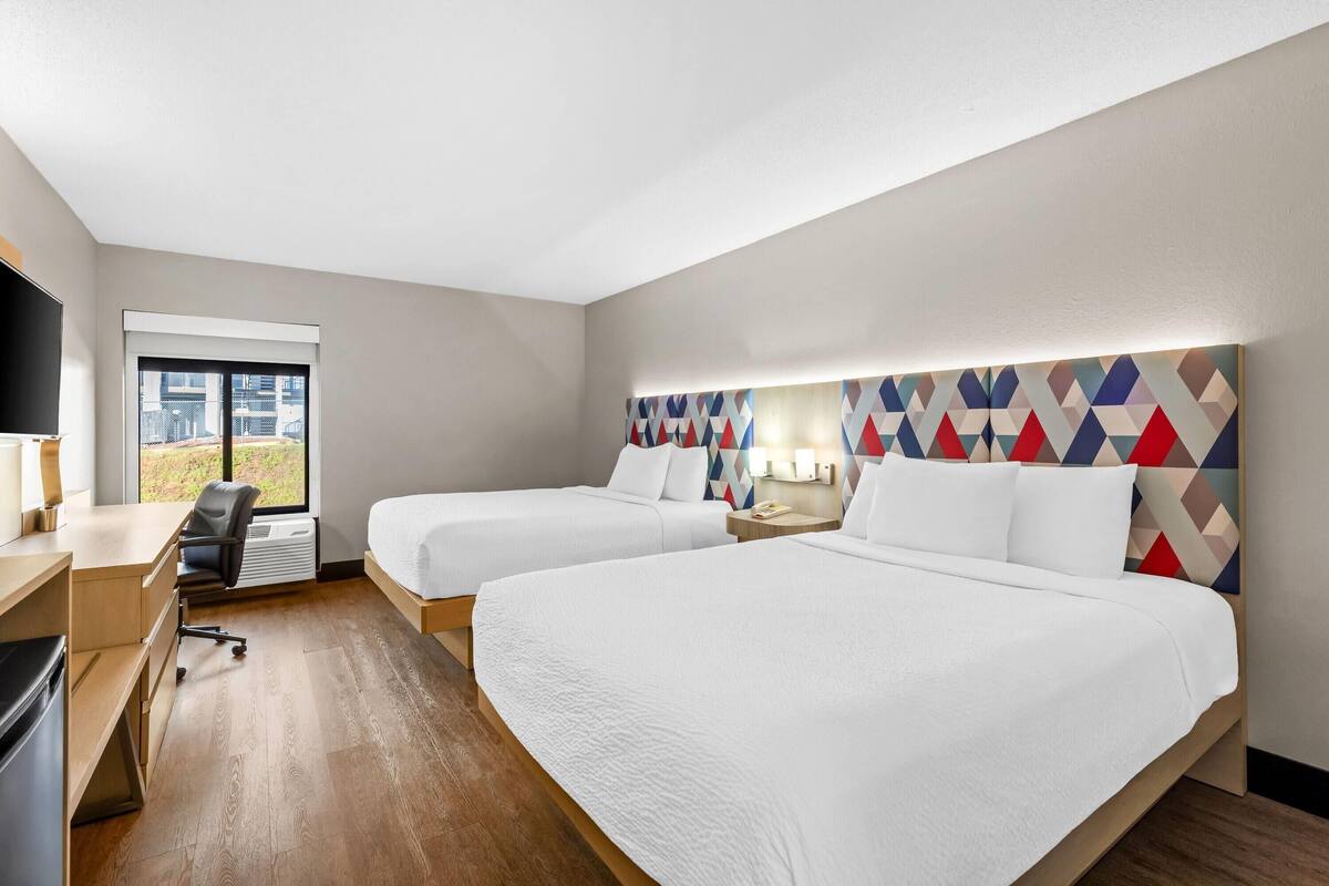 Habitación de hotel con dos camas, un escritorio, una silla y un ventanal grande.
